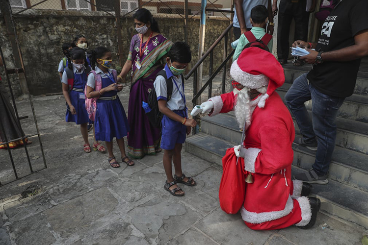 مردی با لباس بابانوئل دمای بدن دانش آموزان را هنگام رسیدن به مدرسه بررسی می کند. بمبئی، هند
