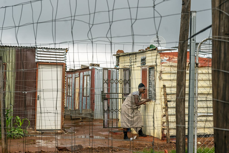 زنی که در سکونتگاه  ولاکفونتین زندگی می‌کند، پنجره‌اش را هنگام باران می‌بندد. ژوهانسبورگ، آفریقای جنوبی