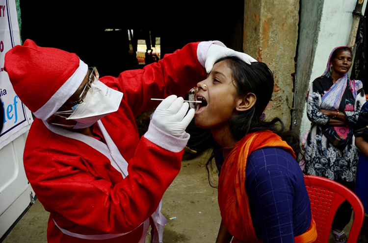 یک کارمند پزشکی که لباس بابا نوئل پوشیده است در بخش اورژانس در حال نمونه برداری از بیماران احتمالی می باشد. کلکته، هند
