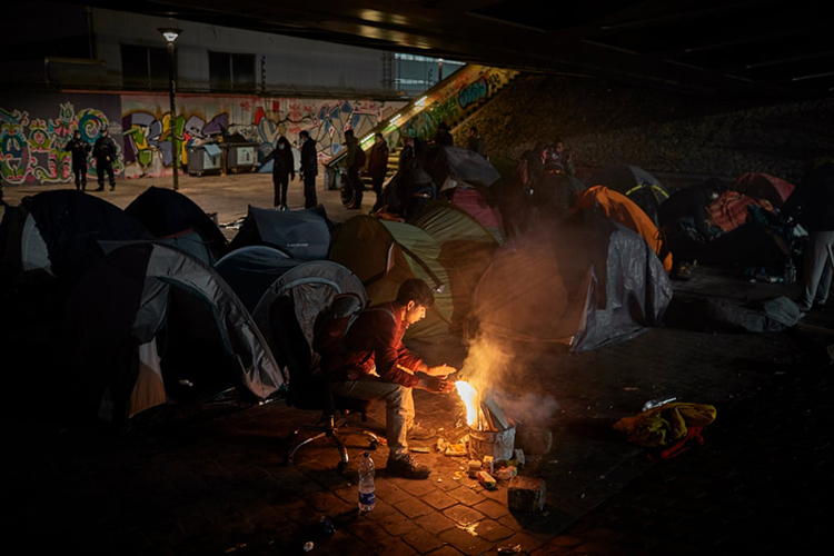 مهاجر افغان برای گرم شدن دور آتش می نشیند، در حالی که یک کمپ موقت در حومه پاریس توسط مقامات شهری و پلیس تخلیه می شود. پاریس، فرانسه