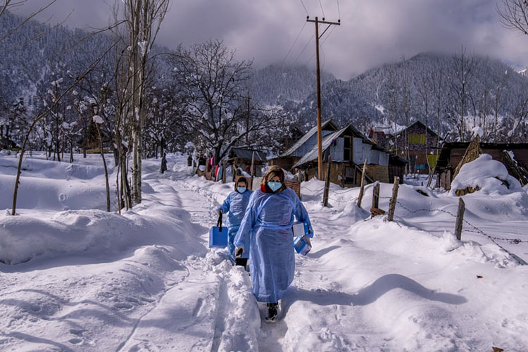 بودگام، هند<br />کارکنان مراقبت‌های بهداشتی کشمیری در بادگام در کشمیر تحت کنترل هند، هنگام راه رفتن در جاده‌ای پوشیده از برف، واکسن حمل می‌کنند.