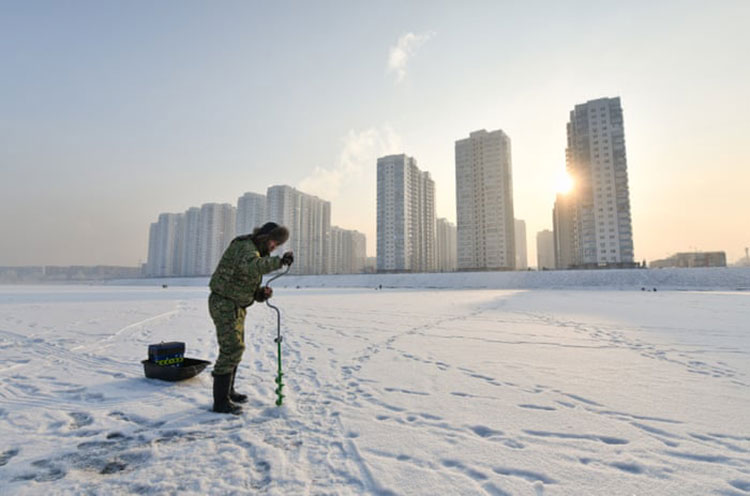 مردی قبل از ماهیگیری در یخ یکی از کانال‌های رودخانه ینی‌سی سوراخ می‌کند.<br />کراسنویارسک، روسیه