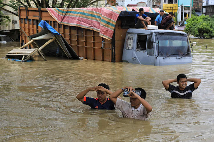 مردم از کنار یک کامیون گیر کرده در آب های سیل در شمال آس در پی بارش شدید باران در منطقه عبور می کنند.<br />منطقه Lhoksukon، اندونزی