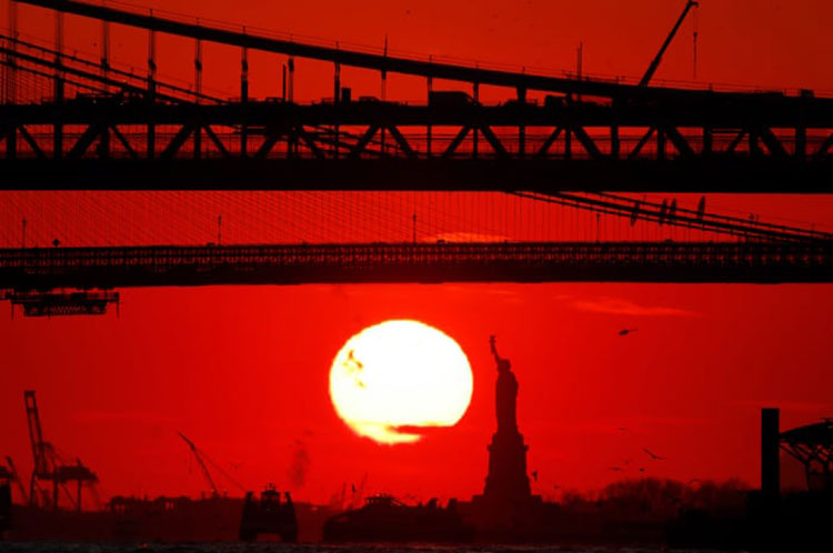 خورشید در پشت مجسمه آزادی، پل بروکلین و پل منهتن قرار دارد.<br />نیویورک، ایالات متحده آمریکا