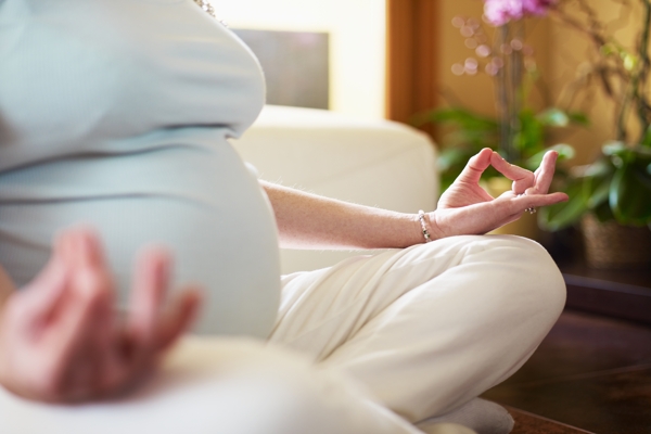 cropped view of italian 6 months pregnant woman sitting with crossed legs doing yoga exercise at home. Horizontal shape, narrow focus
