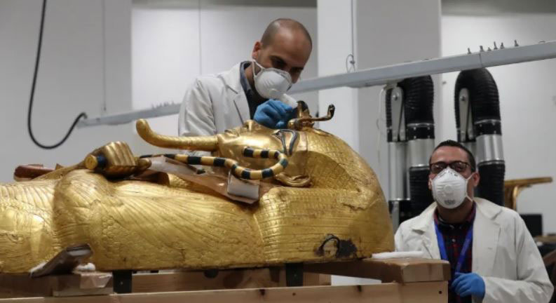 باستان شناسان ماسک زده مصری در حال گشودن تابوت طلایی توت عنخ‌آمون فرعون مصر در موزه ملی مصر در شهر قاهره