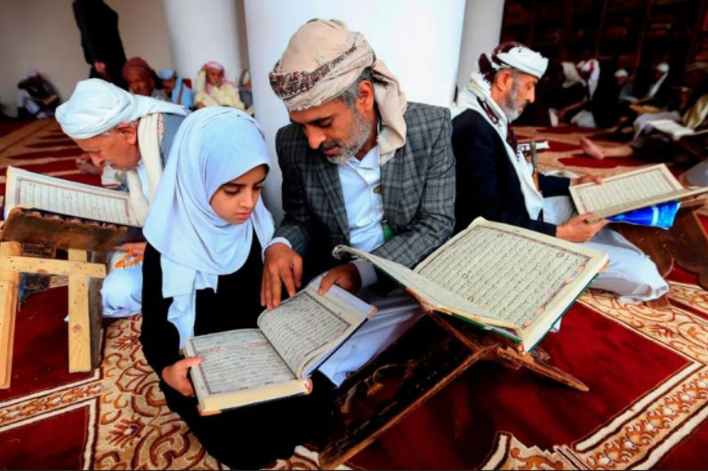 پدر و دختر یمنی در حال قرائت قرآن در مجالس ختم قرآن به مناسبت ماه رمضان در مسجدی در شهر صنعا