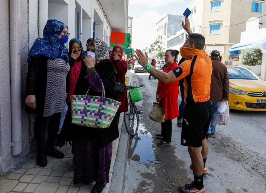 عبدالحق اتیلی داور تونسی هندبال در حال صدور کارت آبی برای زنانی که با نقض فاصله گذاری اجتماعی در بیرون یک مغازه تحمع کرده اند